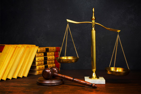 Golden scales of justice beside a gavel and a row of law books on a wooden desk.